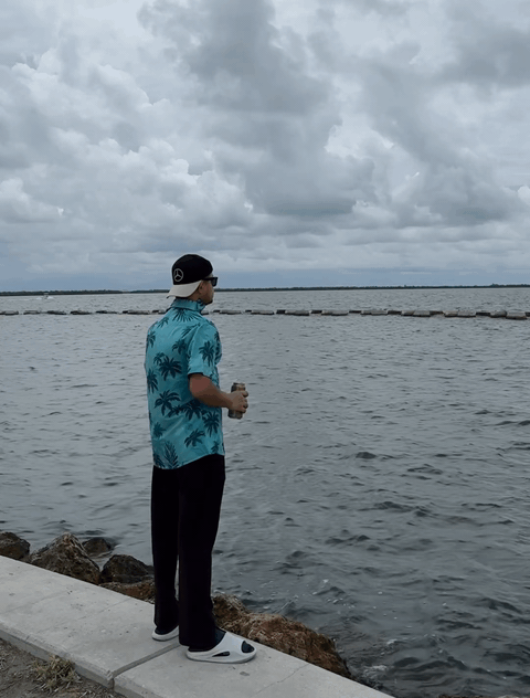 A person standing on a rocky shoreline, looking out over the water beneath an overcast sky.